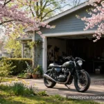 Spring Tune-Up: 8 Insurance Items to Check Before Your First Ride of the Season A motorcycle parked outside a garage on a bright spring morning with blooming trees nearby